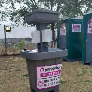 A handwashing station with portable plastic toilets on the background